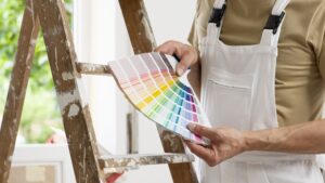 A painter standing by a ladder with painting samples in his hands